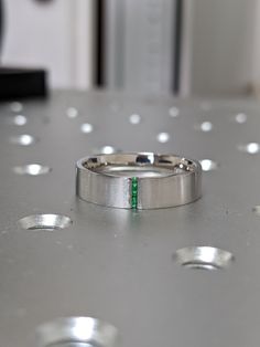 a wedding ring with a green stripe on it sitting on top of a metal table