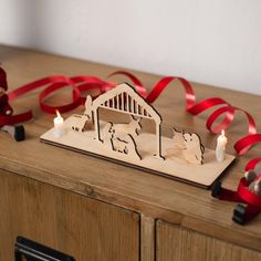 a wooden nativity scene with candles and red ribbon on a table next to it