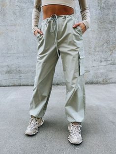 DETAILS: Our Logan Athletic Cargo Pant have an oversized fit with a soft nylon fabric. These cute bottoms have a ribbed stretchy band for a comfortable fit around the waist and there is also a self tie string to synch the waist. There are two side pockets, one flap pocket on the pant leg, and the bottom of the pants have a self tie string to synch it tighter around the ankle. Runs true to size but has an oversized look. CONTENT & CARE: SELF: 100% Polyester. SIZE & FIT: Model is 5'6" The model is Casual Bottoms With Cargo Pockets And Paperbag Waist, Sporty Cargo Style Pants For Spring, Casual Nylon Joggers With Drawstring, Sporty Khaki Bottoms For Spring, Casual Parachute Pants With Functional Drawstring For Spring, Spring Athleisure Cargo Pants With Drawstring, Sporty High-waisted Parachute Pants, Sporty Solid High-waisted Parachute Pants, High-waisted Drawstring Parachute Pants