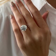 a woman's hand with a diamond ring on her left hand, wearing a white shirt