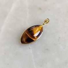 ITEM DESCRIPTION: >>The pendant is made from Solid 14K Yellow Gold. Gemstone used is absolutely natural and ethically sourced. >>Natural Tiger Eye in cabochon marquise shape with bezel setting is studded on it with utmost precision. >>This is a minimalist design and is absolutely hassle-free and everyday jewelry. Gem: Tiger Eye Gem size: 11x21 mm Gem weight: 9.31 carats Gold purity: 14K (58.33% approx.) Gold weight: 0.56 grams Gross weight: 2.42 grams The Gold purity is guaranteed and it comes w 14k Gold Gemstones With Bezel Setting For Gift, Fine Jewelry Cabochon Gemstone Pendant, Polished 14k Gold Amber Jewelry, 14k Gold Amber Jewelry With Polished Finish, Gold Cabochon Teardrop Pendant, Gold Cabochon Teardrop Pendant Jewelry, Teardrop Pendant Jewelry With Bezel Setting, Gold Cabochon Gemstones For Anniversary, Gift Jewelry Teardrop Pendant With Bezel Setting