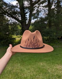 This fedora makes a great addition to any wardrobe. The warm brown material burns a gorgeous shade of dark brown allowing the design to stand out. Cattails are are intricately burned by hand with a pyrography machine. This cattail design is burnt on the front of the crown. All my designs are original and completely freehanded. For a beautiful finishing touch the hat is adorned with a faux leather black hatband. Hat Materials: 65%cotton 35% polyester Hat fits most women with an adjustable tie band inside *Disclaimer* Colors may vary slightly from screen to screen Brown Country Style Felt Hat For Outdoor, Brown Curved Brim Sun Hat For Outdoor, Western Brown Straw Hat, Brown Cap Felt Hat For Rodeo, Brown Felt Hat With Short Brim For Outdoor, Brown Felt Cap For Rodeo, Brimmed Felt Hat For Outdoor Spring Activities, Fitted Brown Felt Hat For Outdoor, Spring Brimmed Felt Hat For Outdoor