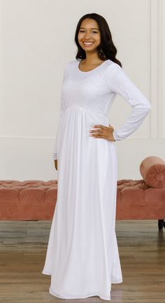 a woman standing in front of a couch wearing a white dress and smiling at the camera