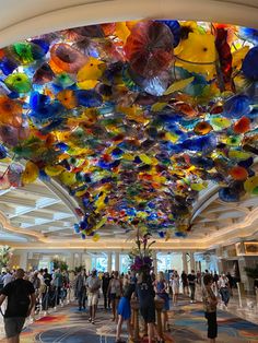 the ceiling is made up of multicolored blown glass flowers and people are walking around