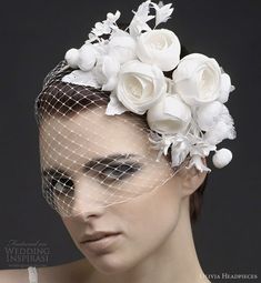 a woman wearing a veil with white flowers on it's head and veil over her face