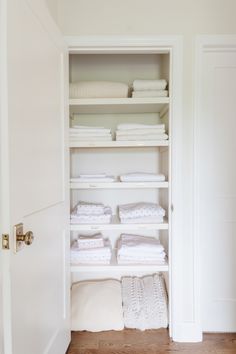 an open closet with folded towels and folded blankets on shelves in the corner, next to a door