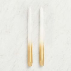 two gold and white candles on a marble surface