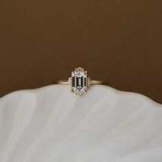 an emerald cut diamond ring on top of a white shell