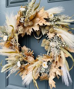 a wreath with dried flowers and feathers hanging on a blue front door, ready to be decorated