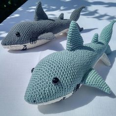 two crocheted stuffed sharks sitting on top of a white cloth covered tablecloth