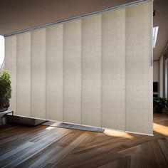 a room with wooden floors and a large window covered in beige fabric roller shades that are open to let light into the room