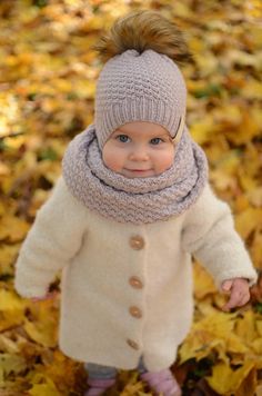 a baby wearing a hat and scarf standing in leaves