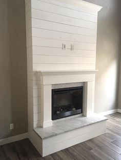 an empty fireplace with white paint on the mantle and wood floors in a living room