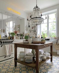 a chandelier hanging from the ceiling in a kitchen next to a table with plates on it