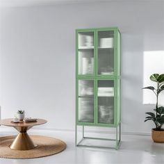 a green cabinet sitting in the middle of a room next to a table and potted plant