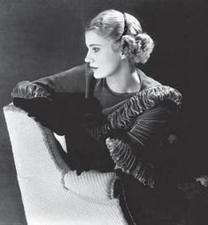 a black and white photo of a woman sitting in a chair with her hand on the arm