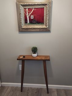 a small wooden table with a potted plant on it in front of a painting