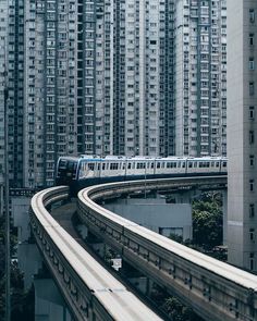 a blue and white train traveling through a large city next to tall buildings on top of each other