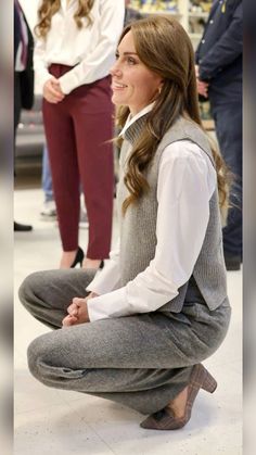 the young woman is sitting on the floor in her pants and sweater vest, smiling