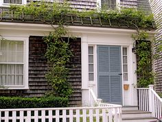 a white picket fence in front of a house with blue shutters and green ivy growing on it