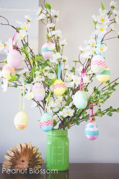 an easter egg tree in a green vase with flowers and eggs hanging from the branches