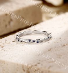 a white gold ring with blue sapphires on top of a marble slab in the sunlight