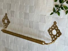 a gold towel rack on a white tiled wall next to a green leafy plant