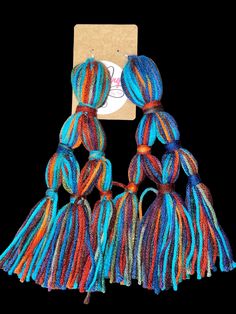 three multicolored yarns are hanging from a string on a black background with a tag