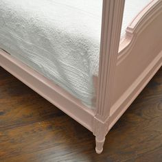 a pink bed frame with white sheets and wood flooring on the bottom part of it