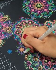 a woman's hand holding a marker and writing on a coloring book with colorful designs