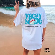 a woman standing on top of a beach next to the ocean holding up her peace sign