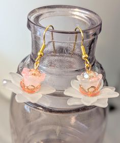 two flower shaped earrings sitting on top of a glass jar with gold earwires