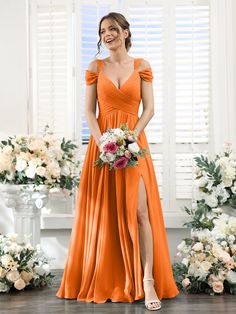 a woman in an orange bridesmaid dress standing next to flowers and holding a bouquet