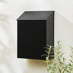 a black box mounted to the side of a white wall next to a potted plant