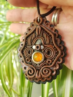 a hand holding a brown necklace with an orange stone in the center and swirls on it