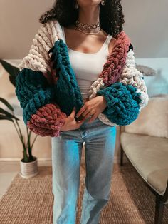 a woman standing in front of a couch wearing jeans and a jacket with multicolored crochet