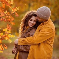 a man and woman embracing in front of autumn leaves