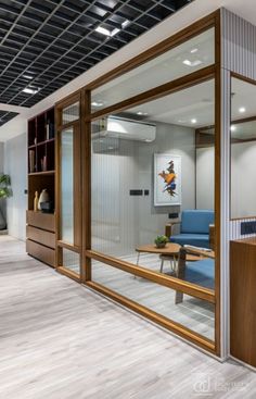 an office with glass walls and wooden furniture in the foreground is a blue chair