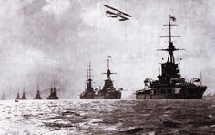 several ships in the water with one plane flying above them and another boat below it