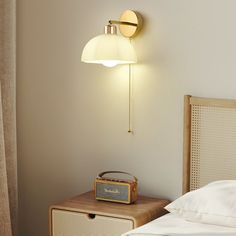 a lamp that is on the side of a wall next to a night stand and bed