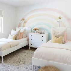 two white beds in a bedroom with a rainbow painted wall behind them and a rug on the floor