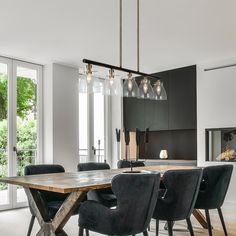 a dining room table with black chairs and lights hanging from it's center point