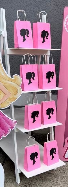 pink shopping bags with black silhouettes on them in front of a barbie doll display