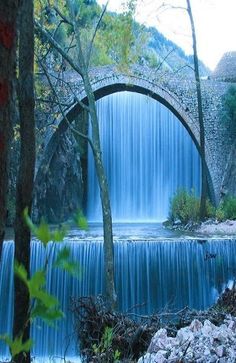 a waterfall with a bridge over it in the middle of trees and rocks near by