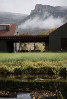 a house sitting on the side of a lush green field next to a body of water