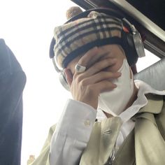 a man wearing a hat and holding his face to his nose while sitting in the back seat of a car