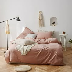 an unmade bed with pink sheets and pillows in a white room next to a wooden floor