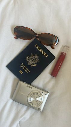 a passport, sunglasses, camera and lipstick on a bed