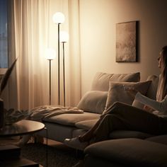 a woman sitting on a couch in front of a window reading a book at night