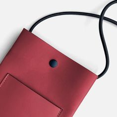 a red leather purse with a black cord hanging from it's side on a white surface